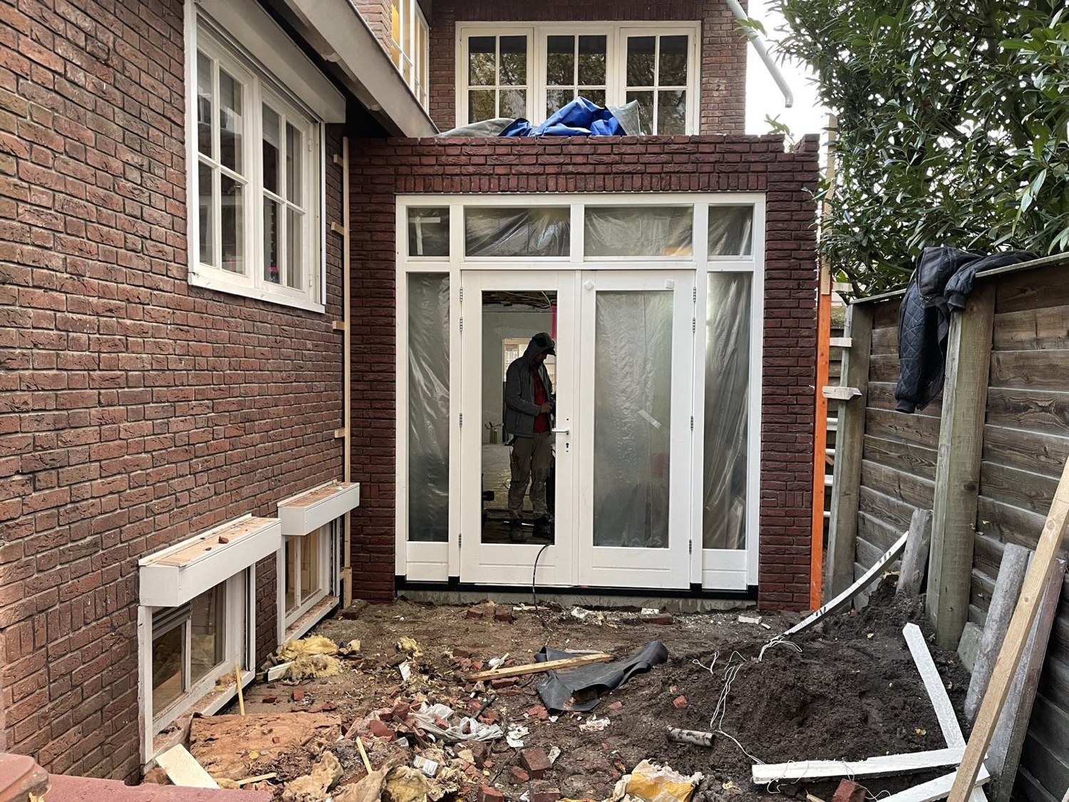 Aanbouw met rode baksteen en klassieke witte openslaande deuren, bijna opgeleverd