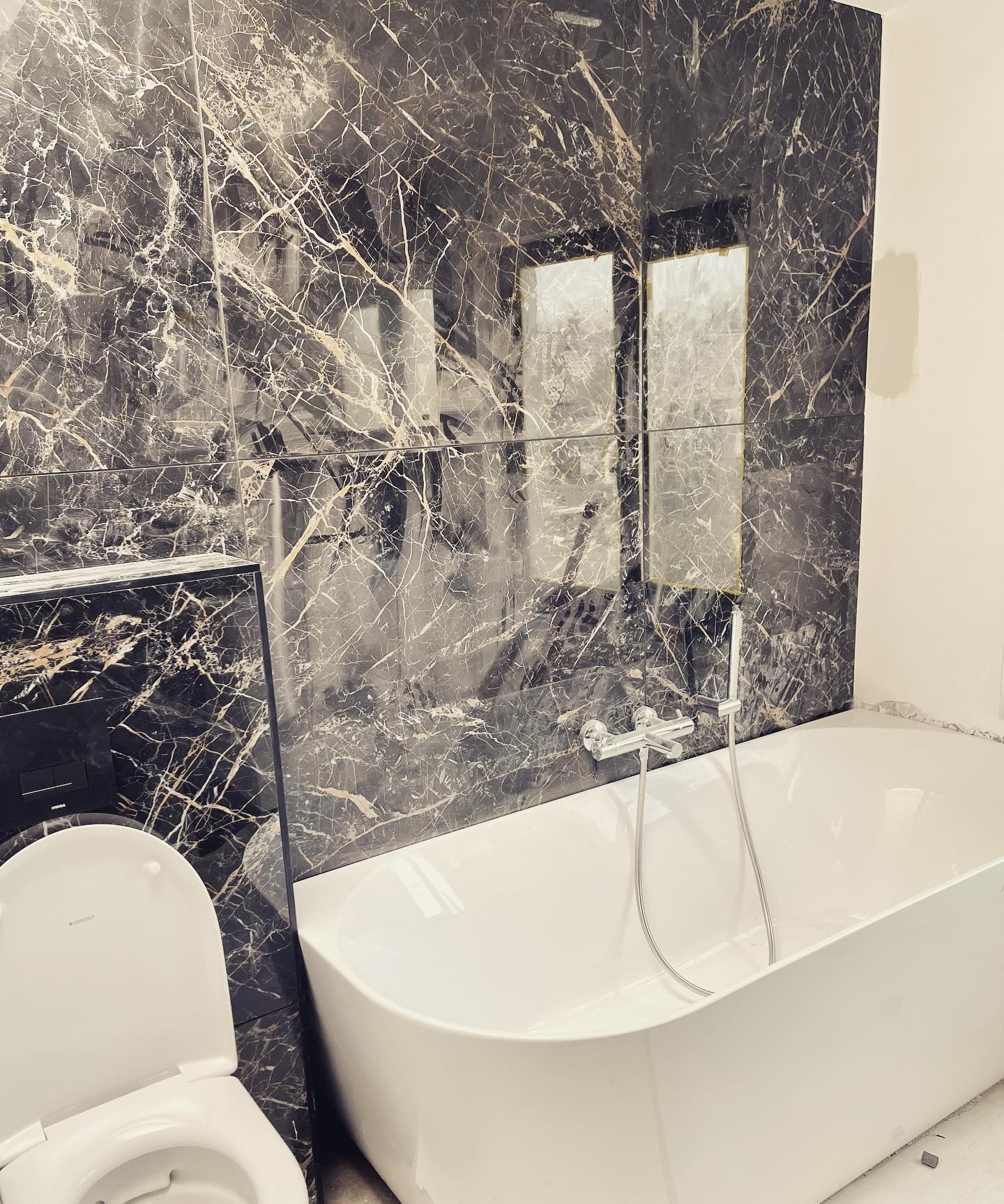Badkamer met zwart marmer op de wand en een vrijstaand bad