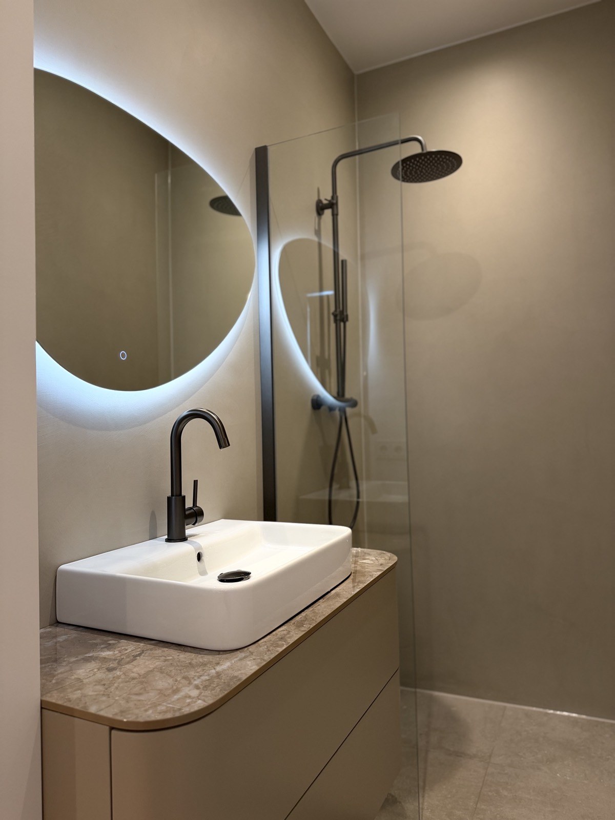 Badkamer met ronde LED-spiegel, zwart sanitair en microcement wanden