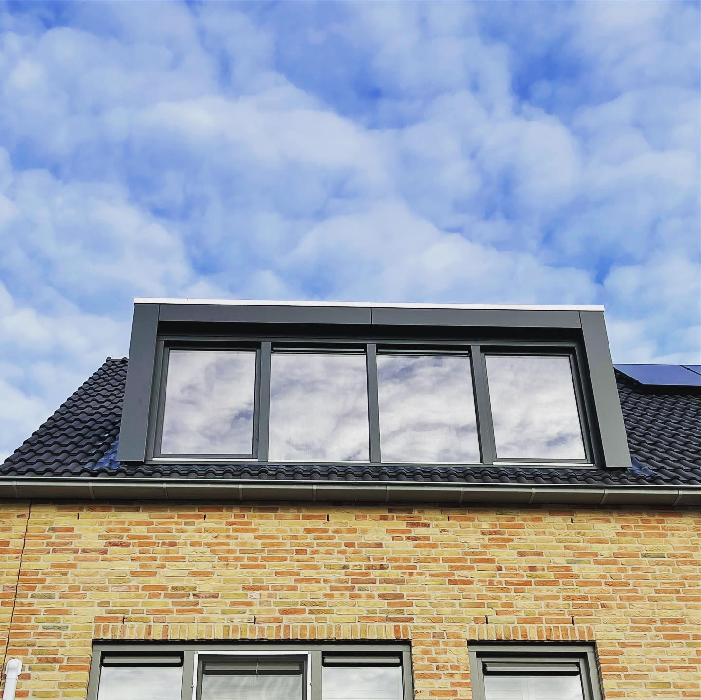 Antracieten dakkapel op een woning in Rosmalen tegen een wolkenlucht