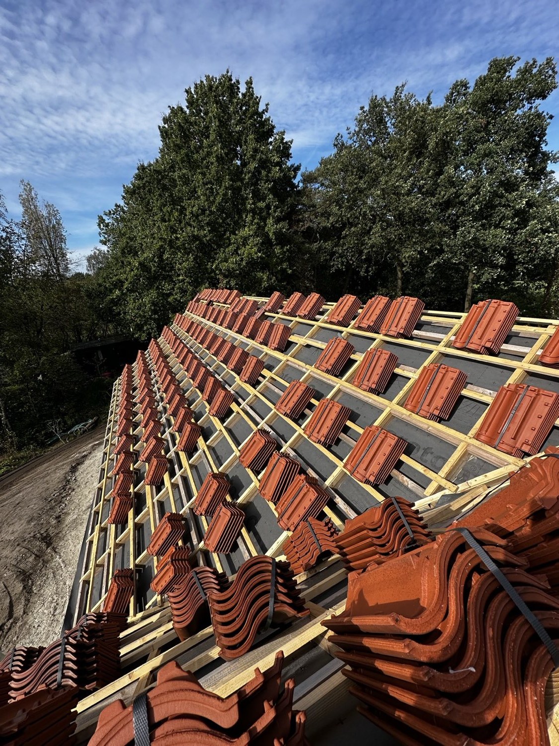 Dakpannen klaargelegd op de panlatten van een dak in aanbouw tegen een blauwe lucht