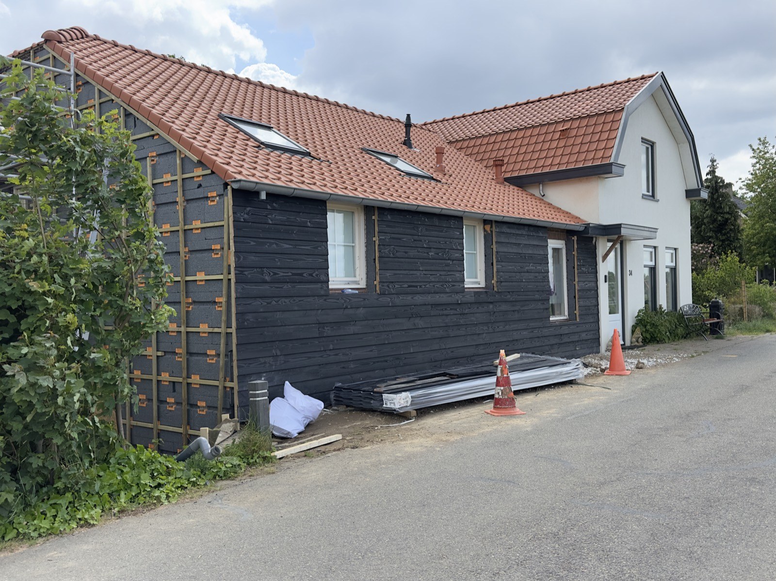 Zijgevel van een woning met nieuwe zwarte houtbekleding en rode dakpannen