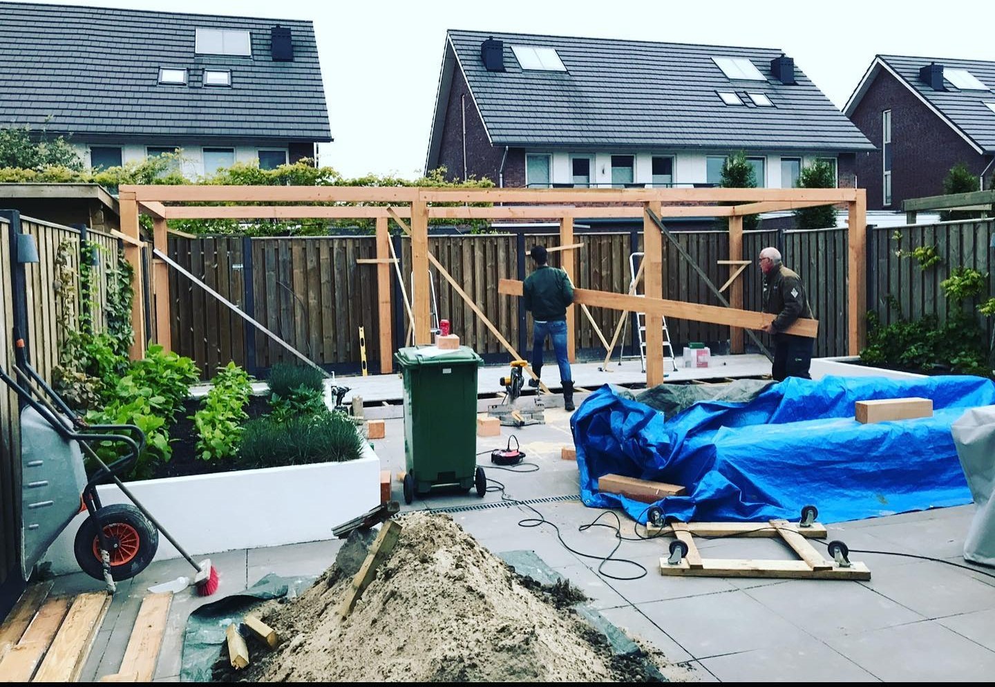 Twee vaklieden bouwen een houten overkapping in een achtertuin