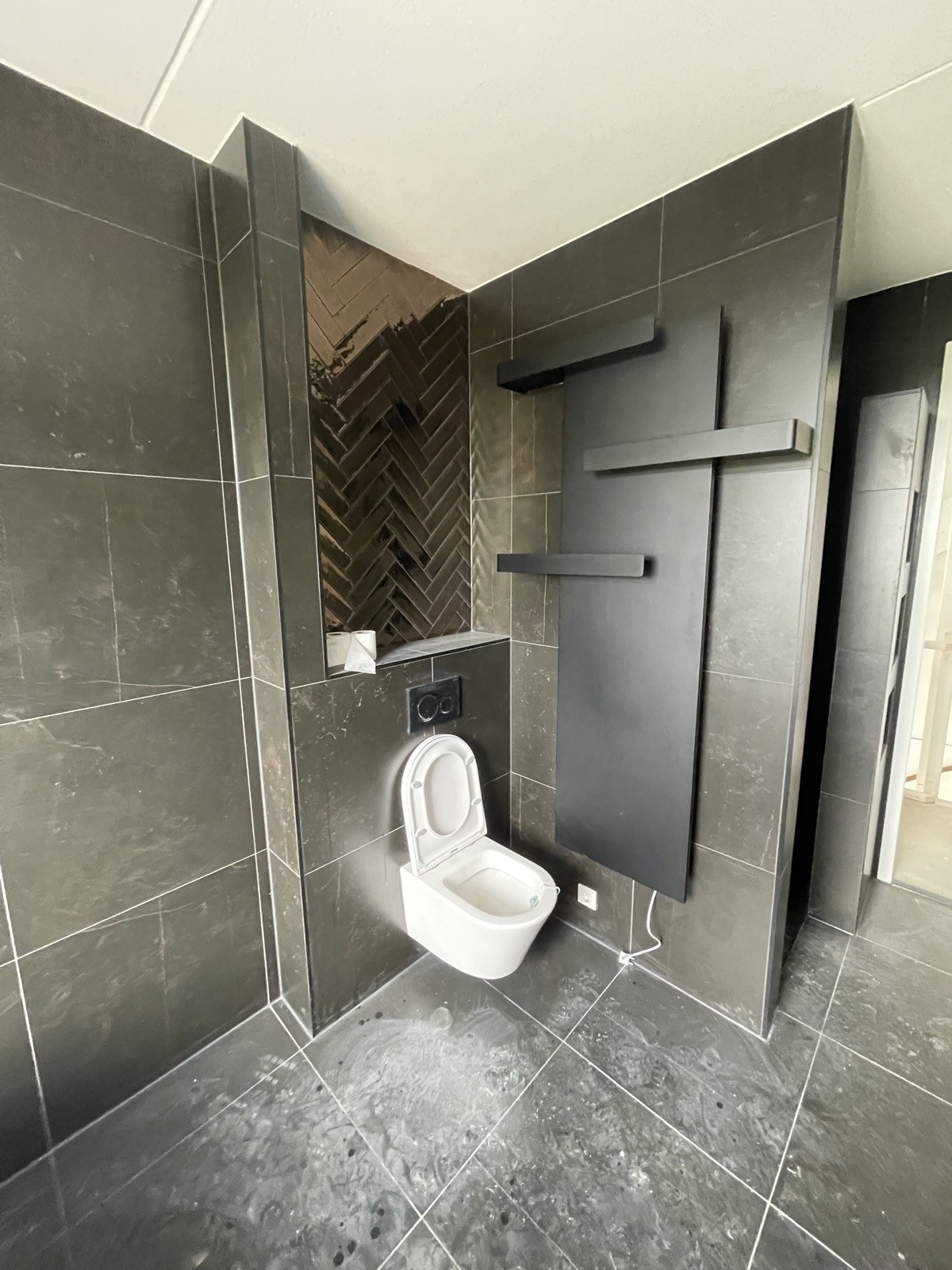 Toilet met donkere tegels, visgraatnis en designradiator