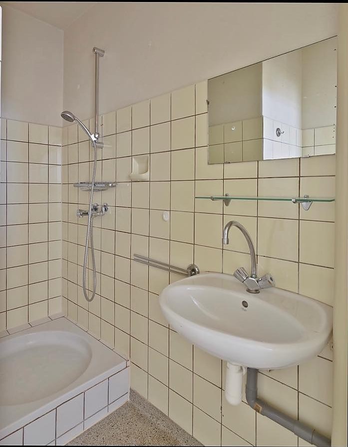 De badkamer voor de renovatie, met beige tegeltjes en een ligbad